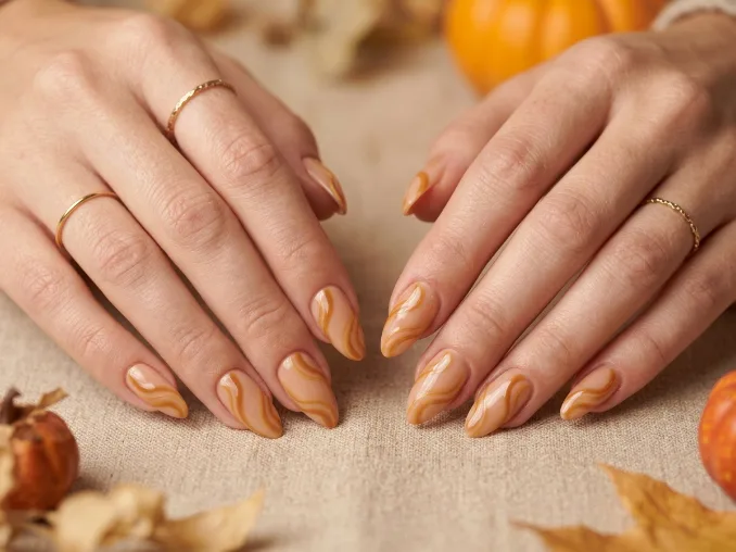 Caramel swirl fall nail designs for 2026 on nude almond-shaped nails.